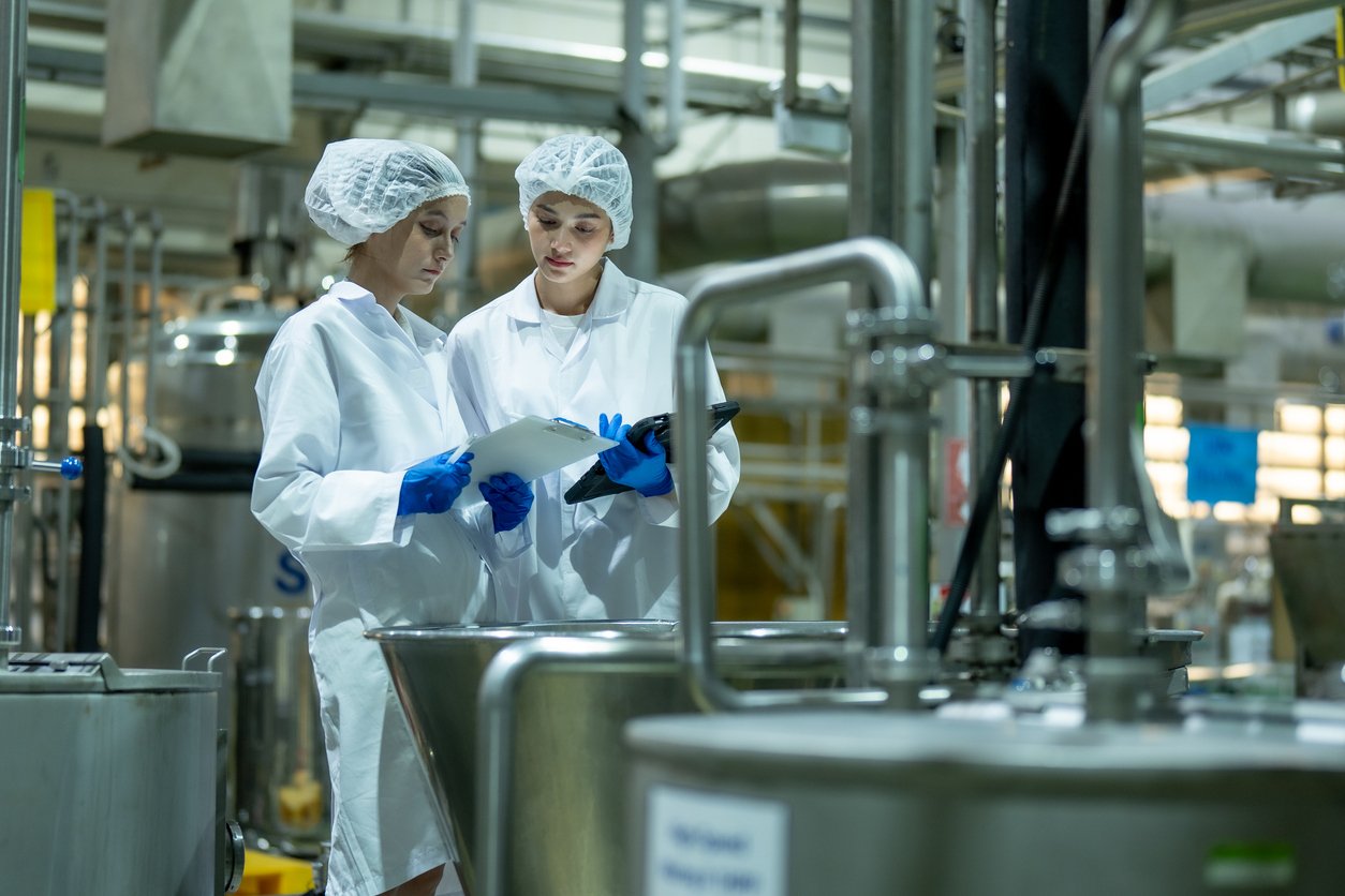 two women with lab clothing on studying chemical mixing tank